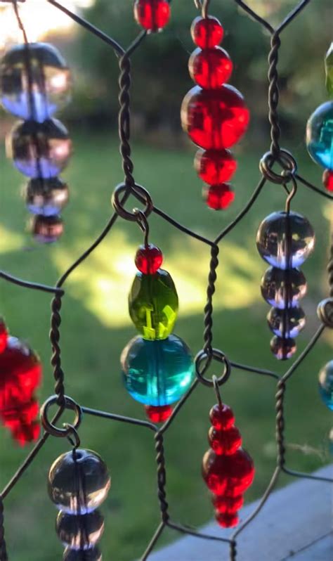 Colorful Glass Beads Hang From A Chain Link Fence In Front Of A Grassy