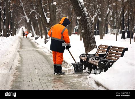 Communal Services Worker In Uniform With A Shovel Clears Snow On A