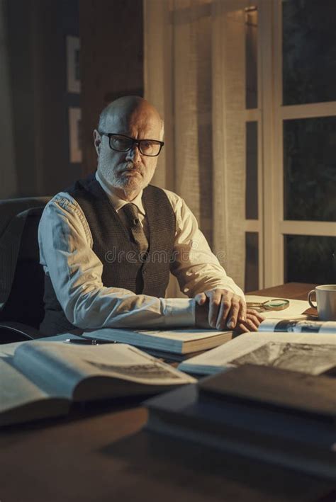 Profesor Confiado Sentado En El Escritorio Y Posando Imagen De Archivo