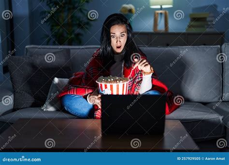 Hispanic Woman Eating Popcorn Watching A Movie On The Sofa Pointing