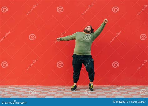 Charismatic Overweight Young Man In Casual Clothes Dancing On Red Wall