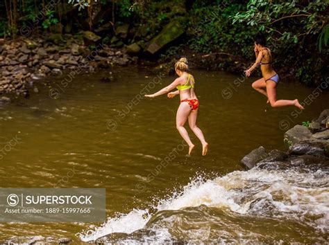 Two Women Wearing Bikinis Cliff Jumping From The Top Of One Of The Twin