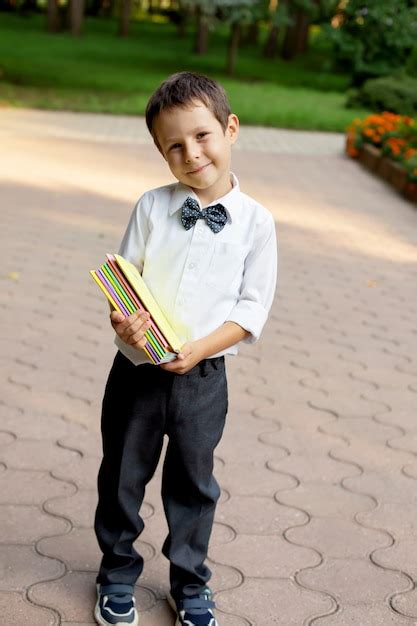 Um lindo menino de escola em uma camisa branca e calça cinza segurando