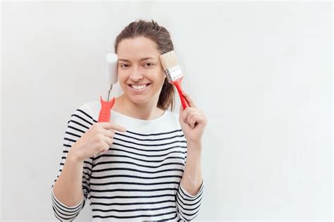 Premium Photo Young Woman Painting The Wall With Paint Roller And Brush