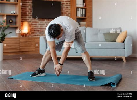 Homme asiatique mature actif faisant des exercices et étirant les jambes muscles à la maison