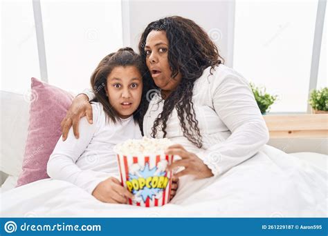 Mother And Young Daughter Eating Popcorn In The Bed In Shock Face Looking Skeptical And