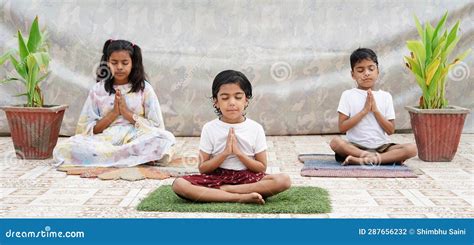 Three Indian Little Kids Doing Meditate Yoga Asana On Roll Mat At Home