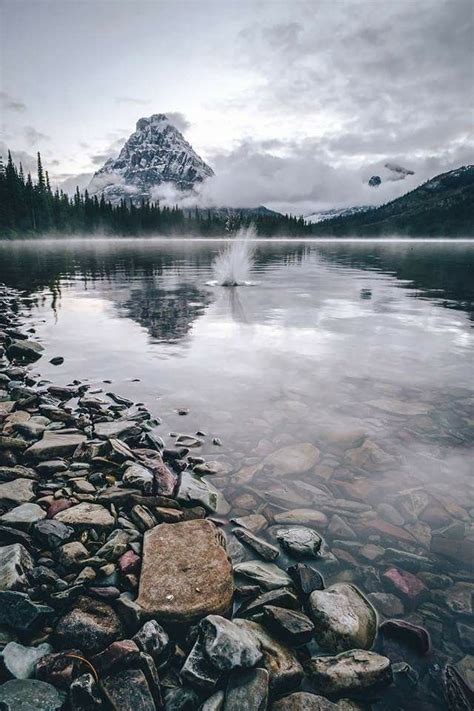 A Rocky Shore With Rocks And Water In The Foreground Mountains In The