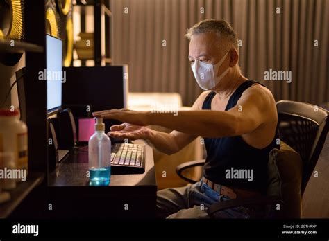Mature Japanese Man With Mask Using Hand Sanitizer While Working