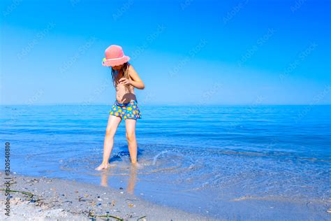 Child girl in summer straw hat is dancing happy barefoot in shallow sea ...