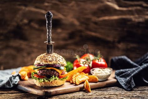 Knife Stabbed In A Hamburger With Potato Wedges On A Side In A Dark