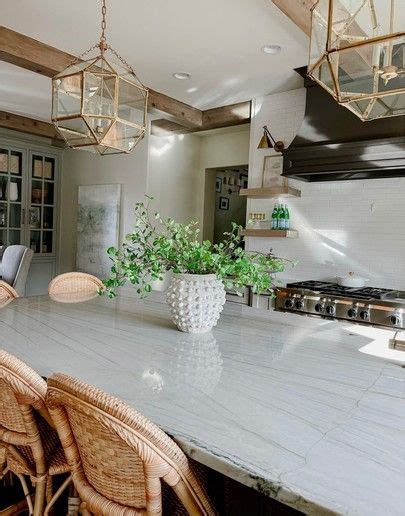 A Kitchen With A Marble Counter Top Next To A Potted Plant On The Island