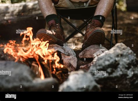 Man In Boots Warms His Feet By The Fire At Camping Site Cropped Shot