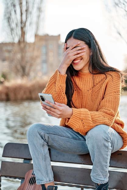 Joven latina mirando su teléfono inteligente con la mano sobre la cara cubriendo los ojos con