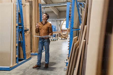 Carpenter Standing With Ring Binder In Front Of Shelves With Wooden