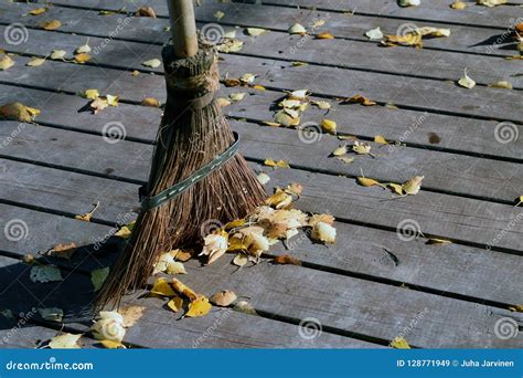 Sweeping A Wooden Patio With A Broom And Removing Autumn Leaves Stock