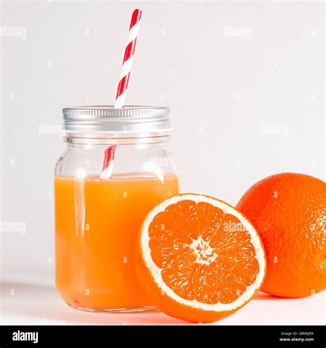 Glass Jar With A Tube With Freshly Squeezed Orange Juice Stands On A White Background Next To