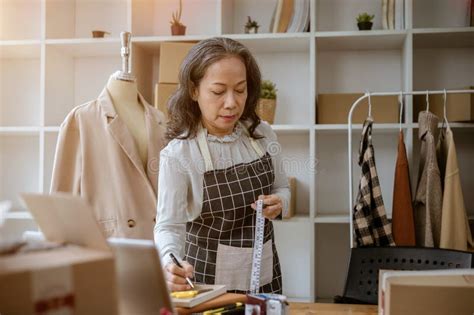 A Mature Asian Female Tailor Is Taking Notes On A Notepad Measuring