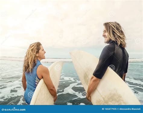 Surfers Couple Running Together With Surfboards On Ocean At Sunset Time