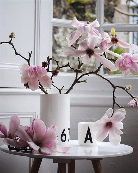 A White Vase Filled With Pink Flowers Sitting On Top Of A Table Next To