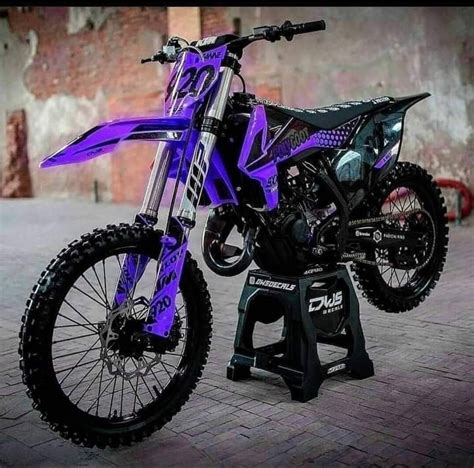 A Purple And Black Dirt Bike Parked On Top Of A Brick Floor Next To A Wall