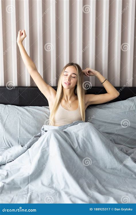 Sleepy Young Woman Waking Up In Bed And Stretching Her Arms At Home