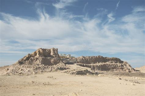 Ancient Desert Ruins Atop Rugged Hill Under Wispy Clouds Stock Photo