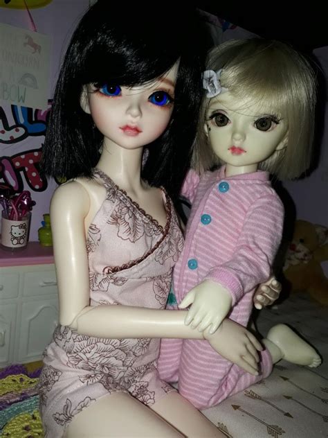 Two Dolls Sitting Next To Each Other On A Bed