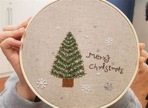 A Person Holding Up A Christmas Tree Embroidered On A Hoop