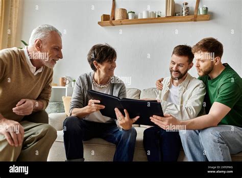 A Gay Couple Sits On A Couch With Parents Sharing Photos From A Photo Album Stock Photo Alamy