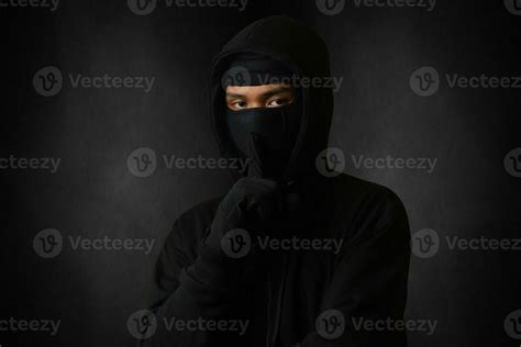 Mysterious man wearing black hoodie and mask standing against dark ...