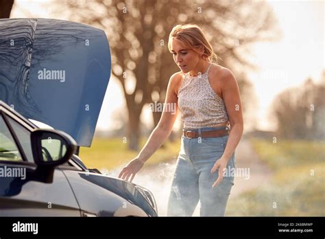 Woman Broken Down On Country Road Looking Under Smoking Bonnet Of Car