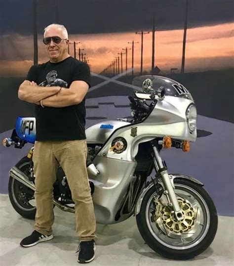 A Man Standing In Front Of A Motorcycle With His Arms Crossed And