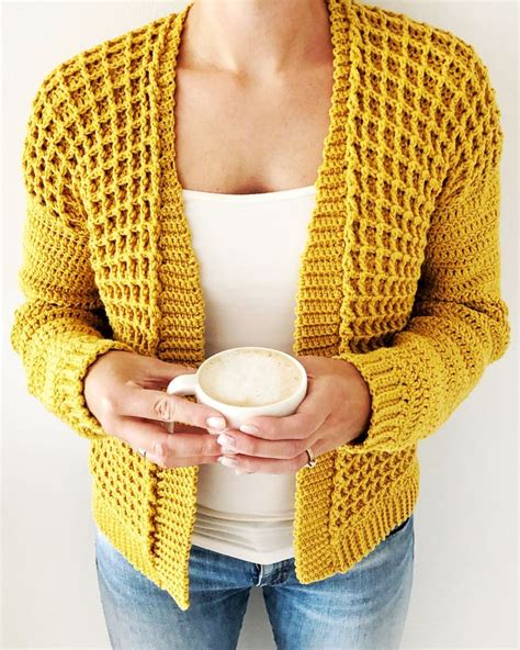 A Woman Wearing A Yellow Knitted Cardigan Holding A White Coffee Cup In Her Hands