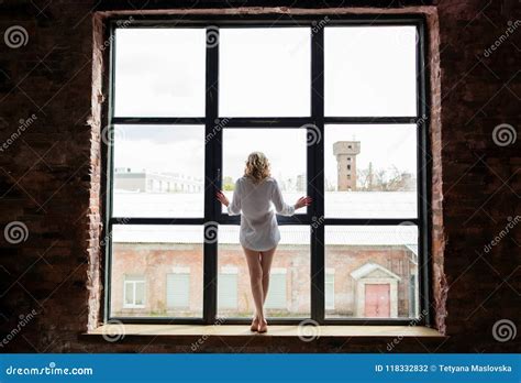 A Beautiful Woman In A Shirt Is Standing On The Windowsill And Looks