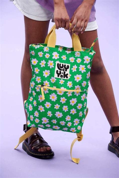 A Woman Is Holding A Green Backpack With White Flowers On It And The