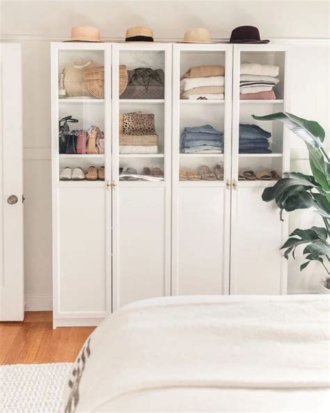 A White Closet Filled With Lots Of Clothes Next To A Bed And Potted Plant