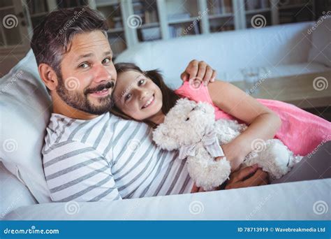 Smiling Father And Daughter Sitting On Sofa With A Teddy Bear Stock