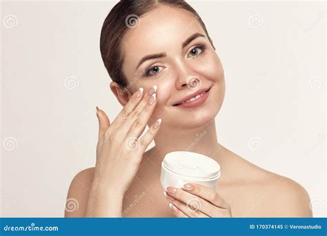 Beautiful Model Applying Cosmetic Cream Treatment On Her Face On White