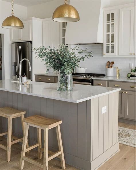 A Large Kitchen With Two Stools In Front Of The Island And Gold Lights