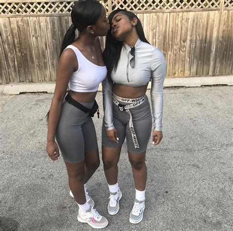 Two Women Standing Next To Each Other In Shorts And Crop Tops One Is Kissing The Others Cheek