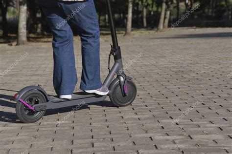 Mujer irreconocible montando su patinete scooter eléctrico en la ciudad