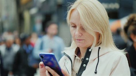 A Sad Middle Aged Woman Uses A Smartphone In A Crowd Of People