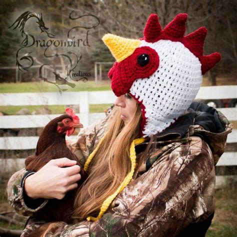 A Woman Wearing A Crocheted Chicken Hat While Holding A Brown And White Rooster