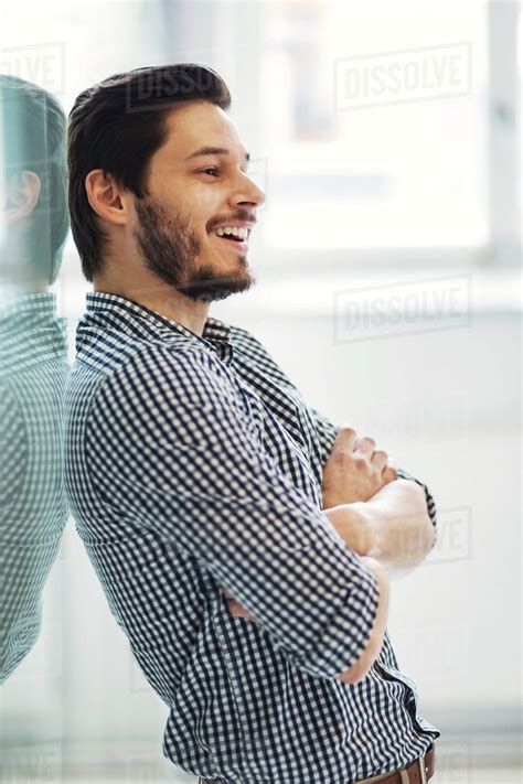 Side View Of Smiling Businessman With Arms Crossed Leaning On Wall In