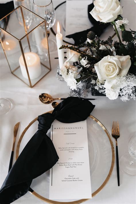 A Table Setting With Black And White Flowers Gold Rimmed Place