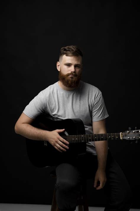 Bearded Musician Playing Acoustic Guitar In A Dark Room Stock Image