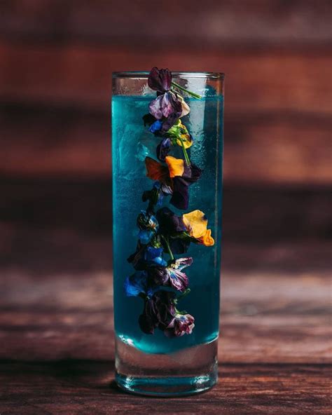 A Tall Glass Filled With Blue Liquid And Colorful Flowers On The Rim