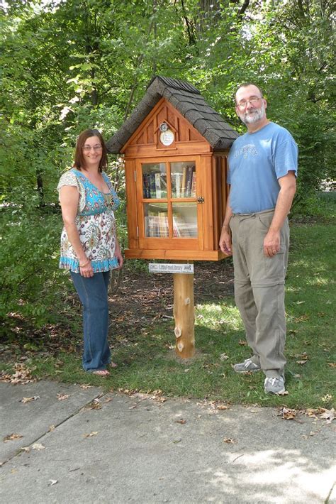 Two People Standing In Front Of A Small Wooden House With A Clock On It