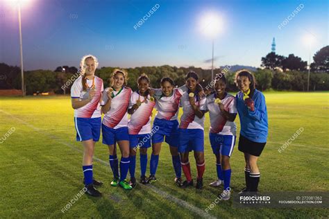 Vista frontal del diverso equipo femenino de fútbol posando con medalla